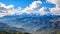 A breathtaking view of a grand mountain range framed by a picturesque sky filled with fluffy clouds., Panoramic view of the