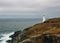 Breathtaking view of a lighthouse on a grass-covered hill by the ocean on a cloudy day