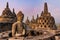 Breathtaking view of the sunrise from the meditating Buddha statue and stone stupas against a bright sun background. The ancient B