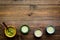 Brew matcha tea. Bowl with powder and cups with beverage on dark wooden background top view copy space