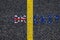 Brexit blue european union EU flag and uk great britain united kingdom flag, over tarmac, road marking yellow paint separating lin