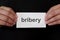 Bribery crime case mug shot concept. Criminal hands holding paper placard with written word in dark black background.