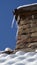 Brick chimney ordains with icicles on snow-covered roof.