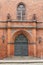 Brick wall of the Church with arched iron door, stained glass window and lanterns. Christmas decorations.