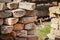 Brick wall corner with sticking out old red bricks and visible grass on the background