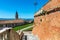 Brick wall, houses and belfry under blue sky in small italian, town