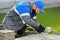 Bricklayer lays paving slabs outside. Working man performs landscaping. Builder lays out sidewalk with stone blocks.