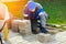 Bricklayer in work clothes sits on sidewalk and lays out paving slabs. Sight of working man in open air.