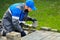 Bricklayer in work clothes sits on sidewalk and lays out paving slabs. Sight of working man in open air.