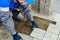 Bricklayer in work clothes sits on sidewalk and lays out paving slabs. Sight of working man in open air.