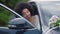 Bridal bouquet lying on car hood with blurred African American bride in white wedding dress sitting inside in slow