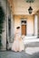 Bride in a beautiful dress with a bouquet of pink flowers stands in an arched corridor near the greenery. Lake Como