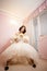 Bride in a beautiful lace dress and long skirt sits on a white vintage chair in anticipation of the groom