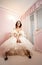 Bride in a beautiful lace dress and long skirt sits on a white vintage chair in anticipation of the groom