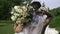 The bride from behind holding a bouquet in one hand while the other is holding a veil over her head.