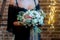 The bride in black dressing gown standing on a loft background with garlands and holds a wedding bouquet