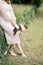 Bride with a bouquet in her hand is leaning against a hedge in the garden. Cropped. Faceless