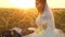 Bride caresses groom with grass stalk in face. happy family is lying in field in rays of beautiful sunset. young woman