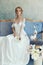 Bride in a chic long dress lying on the sofa couch. White wedding dress on the bride`s body. Beautiful light dress with a long he