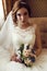 Bride with dark hair in luxurious lace wedding dress with bouquet of flowers