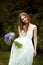 Bride daydreams standing with a violet bouquet in the park