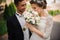 Bride enjoys the scent of a wedding bouquet, the groom stands beside smiling