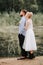 The bride gently hugs the groom from behind on the shoreline. Beautiful newlyweds on the background of the river