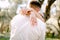 The bride gently hugs the groom in the park, wrapping her arms around his neck, close-up