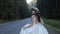 Bride with green crown on the head runing on the road near the forest. Slow motion