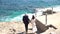 The bride and groom descend on the rocky seashore and hold hands