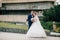 The bride and groom embrace and stroll in the park. A man hugs his beloved, and the girl cheerfully looks at the camera