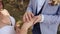 The bride and groom exchange wedding rings against a background of green nature. The groom puts the ring on the arm of