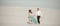 Bride and groom hold hands, smile and walk barefoot in desert. W