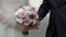 The bride and groom hold hands. Between them a wedding bouquet. Close-up