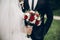 bride and groom holding stylish bouquet of red roses during wedding ceremony. wedding couple reception in park