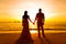 The bride and groom are kept hands on a tropical beach . Silhouette photo at sunset .