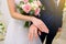 The bride and groom show off their precious gold wedding rings. Bouquet of white and pink roses, neat French manicure of