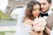 Bride and groom sitting on bench in park, holding hands of each other and bouquet. Groom holding his head on bride`s shoulder and