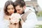 Bride and groom sitting on bench in park, holding hands of each other and bouquet. Groom holding his head on bride`s shoulder and
