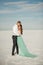 Bride and groom stand barefoot in desert and embrace.