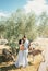 Bride and groom stand hugging under an olive tree near grazing donkeys