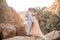 Bride and groom stand and kiss in canyon against background of rocks and palm trees.