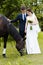 Bride and groom are standing in the park near the horse, wedding walk. White dress, happy couple with an animal. Green background