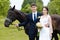 Bride and groom are standing in the park near the horse, wedding walk. White dress, happy couple with an animal. Green background