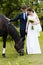 Bride and groom are standing in the park near the horse, wedding walk. White dress, happy couple with an animal. Green background