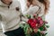 Bride and groom in warm winter clothes holds in hands a rustic wedding bouquet with red and crimson flowers. Close-up.