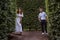 The bride and groom in white clothes hide in a green maze of trees. Newlyweds in a summer park among the foliage