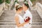 The bride and groom in wreaths stand hugging and kissing on the stairs of the Nativity of the ancient church in Prcanj