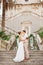 The bride and groom in wreaths stand hugging on the stairs of the Nativity of the Blessed Virgin Mary church in Prcanj