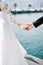 Bride hand touches the palm of groom standing on the pier. Cropped. Faceless